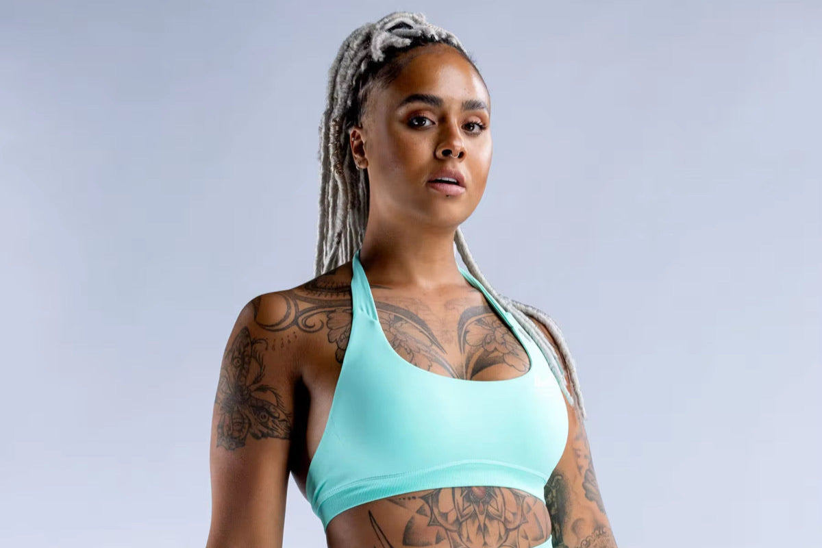 Woman wearing a turquoise sports bra and leggings against a gray background